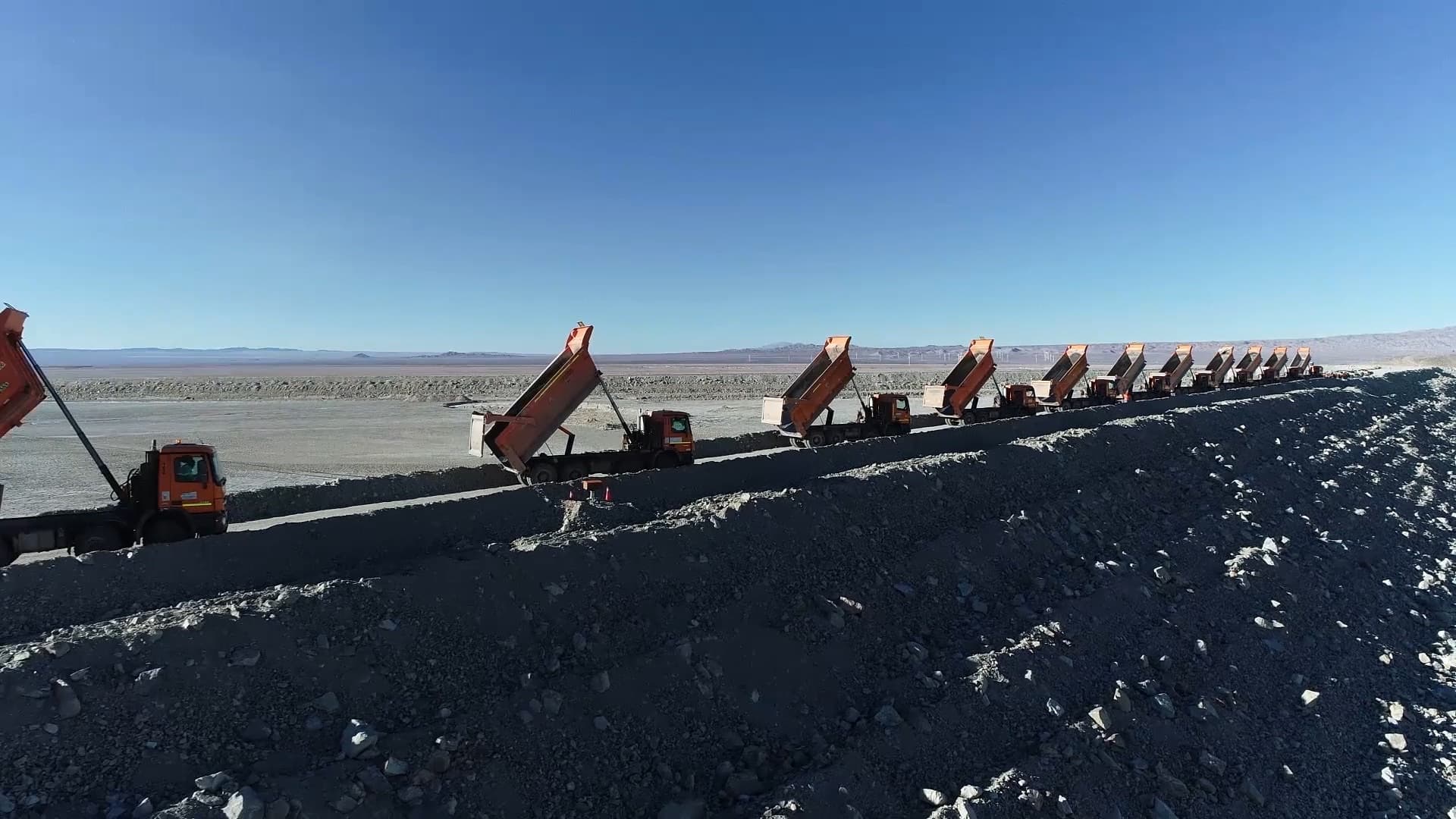 Fila de camiones tolva de CYC descargando material en un camino de faena en el desierto